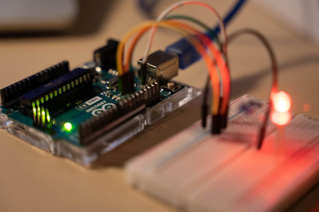 pexels-photo-15470542 Close-up of Arduino microcontroller connected to a breadboard with a glowing LED.