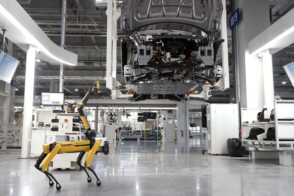 pexels-photo-19319639 A robotic dog oversees an automated car assembly in a high-tech factory setting.